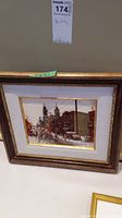 Framed painting showing winter street hockey scene with city buildings and church towers