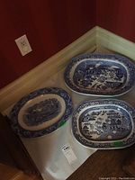 Three blue and white ceramic platters shown together on a covered surface in a corner against a red wall and white baseboard