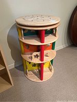 Full view of circular wooden play structure showing three levels, colorful cut-out side panels, and spinning base.