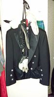 Black formal jacket with decorative silver buttons, flap pockets, and a beige flask in one pocket