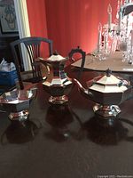 Photo showing the silver plated coffee pot, tea pot, and sugar bowl on a wooden table.