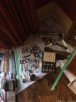 Photo showing assortment of spoons, napkin ring holders, wooden utensils, and kitchen knives spread on floor with a white backing sheet under them.