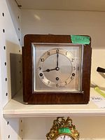 Front view of vintage wooden clock with silver-tone face and Arabic numerals, visible wear on wood.