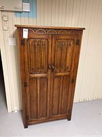 Front exterior view of carved wooden wardrobe with closed double doors and decorative carved top.
