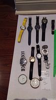 Nine watches arranged on a flat surface including wristwatches and pocket watch, also an Imperial stopwatch with chain