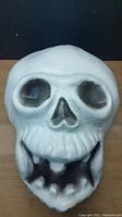 Front view of vintage skull blowmold showing hollow eye sockets, nose and mouth with black shading.