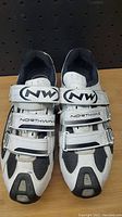 Top view showing white and black cycling shoes with three Velcro straps each, Northwave logos visible on tongue and straps.
