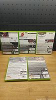 Back side view of five Xbox 360 NHL game cases arranged with three standing in back and two lying flat in front, showing game descriptions and details on the back covers.