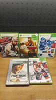 Photo of five Xbox 360 sports games lined up on a wooden surface in front of a black pegboard. The games are UFC Undisputed, UFC Undisputed 2009, NHL 12, Fight Night Round 3 Platinum Hits, and NHL 13.