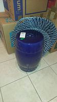 Asian style cobalt blue ceramic garden stool with blue and white woven wall hangings leaning against it on tiled floor, surrounded by cardboard boxes.