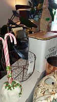 Copper bowl on wire stand next to a white large metal container with wooden lid and candy cane shaped decor.