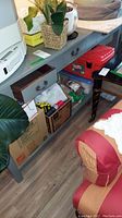 Photo showing the sofa table partially covered with household items on top and under the lower shelf. The table is painted gray with visible wear and three small drawers.