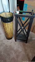 Full view showing two umbrella stands side by side, one round embossed gold and black, one rectangular black frame with glass base