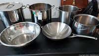 Overview of all pots, colander, and wok laid out on table, showing size and condition