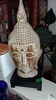 Front view of resin Buddha head sculpture with textured hair and distressed paint finish on black base.