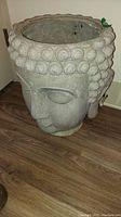 Full side angle view of large Buddha head resin planter on wooden floor, showing detailed facial features and hair curls.