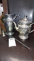 Photo showing the full set including tea pot, pitcher, and candle snuffer on a dark surface.