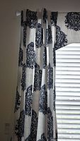Photo of blue and white patterned window treatment curtain panels hanging beside a window with white blinds.