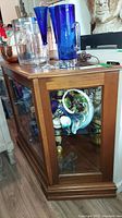 Side view showing the narrow depth and glass side panel with visible display items inside the cabinet