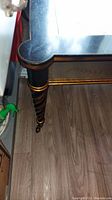 Close-up photo of one corner of the coffee table showcasing the black wooden leg with gold accents and caster wheel attached.