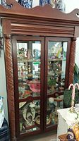 Front view of the wooden display case showing carved side columns, two glass doors, and interior contents on glass shelves.