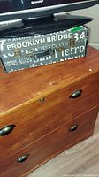 Close-up photo of small decorative suitcase with typography design and metal latch, sitting on wood composite file cabinet surface.