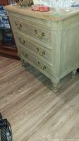Full view of the three drawer wooden dresser showing distressed wood and brass handles.