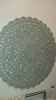 Close-up angle showing the detailed carved floral and geometric pattern on round wood wall art with distressed pale blue-gray finish.