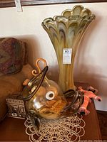 Overall view of art glass vase, fish sculpture, and small decorative figures on table with doily