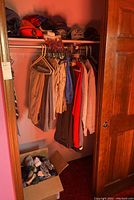 Full view of closet showing ball caps on shelf, slacks and shirts hanging, and box of socks below