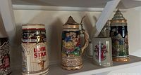 Shelf displaying several collectible international brewery beer steins including Lone Star and others with painted detailed scenes and metal lids.