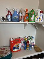 Cleaning products and laundry soaps arranged on a shelf and dresser, with various bottles and folded rags