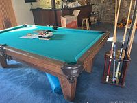Pool table with green felt, oak frame, and cues in holder at right, balls and manual on surface