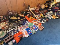 Wide shot showing ticket stubs, foam finger, bobbleheads, mugs and assorted Broncos and Colorado sports items on blue carpet