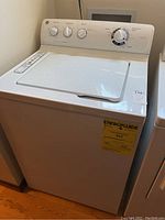 Front and top view of white GE top-load washing machine with closed lid and control panel