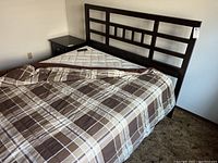 View of queen bed showing dark wood contemporary headboard with rectangular cutout pattern, partially covered adjustable mattress, and bedspread with remote control on bed.