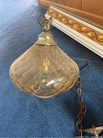 Photo of the mid-century style textured amber glass pendant light with brass chain on blue carpet.