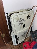 Three mid-century modern style folding tray tables leaning against wall, showing speckled trays with leaf designs and metal legs.