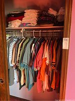 Photo showing men's polo shirts and casual shirts hanging on hangers in a closet with various colors such as green, orange, and multicolors.