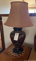 Southwestern style pottery table lamp with fabric shade on table, showing large urn-shaped base with geometric patterns in red, black, and brown.