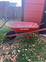 Red True Temper wheelbarrow with dirt and leaves around, showing metal frame, handles and wheel.