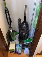 Overall view of vacuum, mop, duster and cleaning supplies clustered together in corner