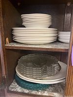 Shelves with stacked white ceramic dinner and smaller plates, clear glass textured edge plates below.