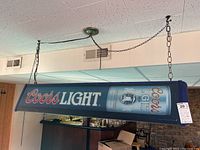 Lighted Coors Light bar sign hanging from ceiling chains, 49x12x10 inches, shows Coors Light branding with bottle image.