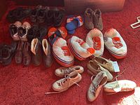 Full view of various shoes including vintage Converse Chuck Taylor All Star sneakers, slippers, boots, and casual shoes arranged on red carpet.