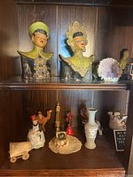 Wide view of wooden shelves with two Asian style ceramic bust figurines, porcelain figurines, miniature wagon, vase and glass plate