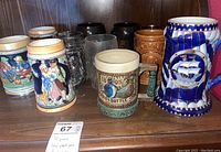 Photo showing 10 assorted vintage glass and ceramic steins on a wooden surface.
