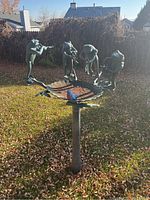 Metal bird bath featuring a basin with a frog and a bird figure sitting on the edge, surrounded by four frogs playing musical instruments.