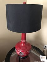 Front view of red ceramic table lamp with black fabric shade on a glass table.