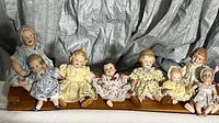 Full view of all 6 dolls seated on wooden display stand showing size and dress variety